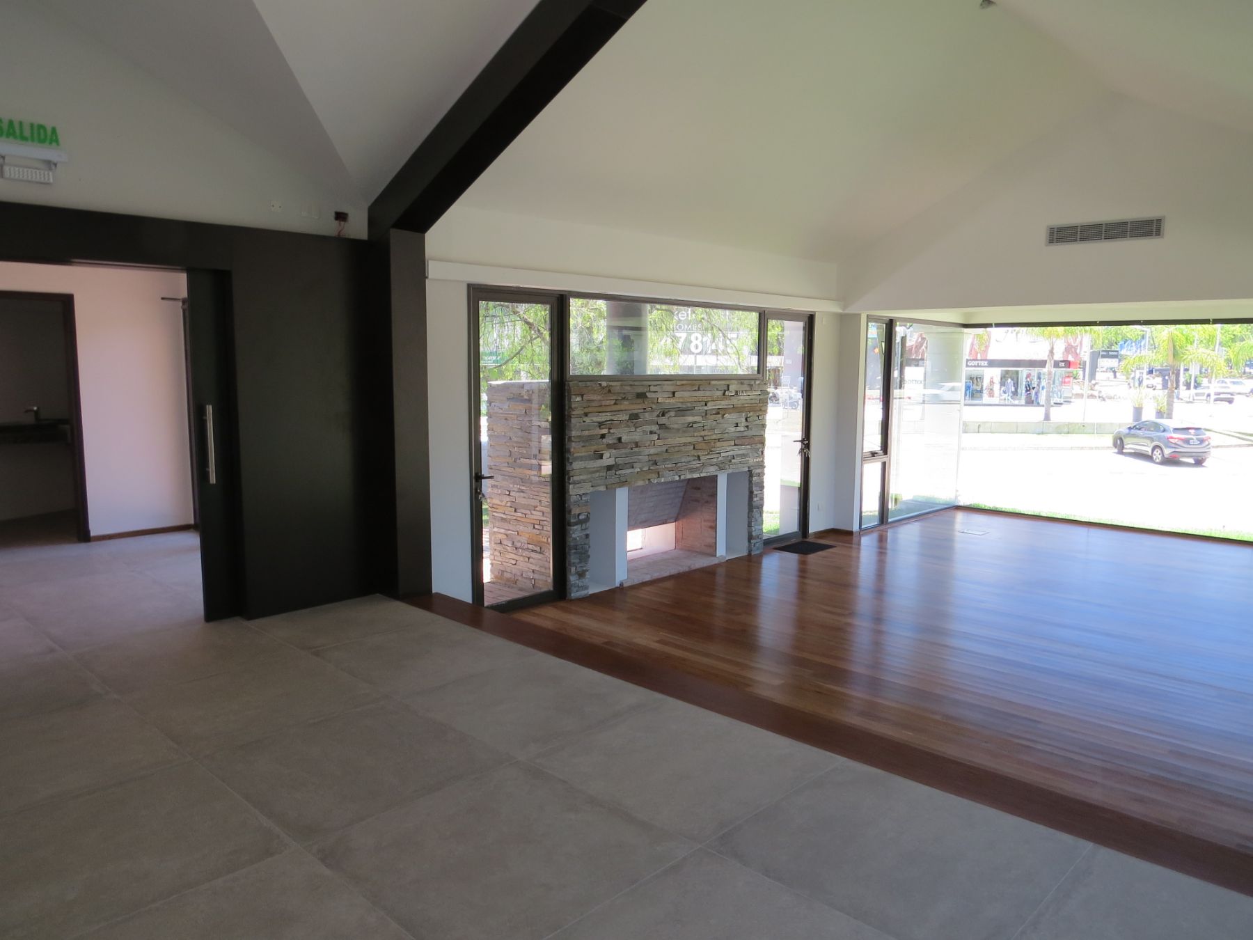 Es una fotografía de la sala principal de la planta alta pero con énfasis en la estufa de piedra. Aún así se aprecian los pisos de lapacho y porcelanato, así como los techos con varias pendientes.